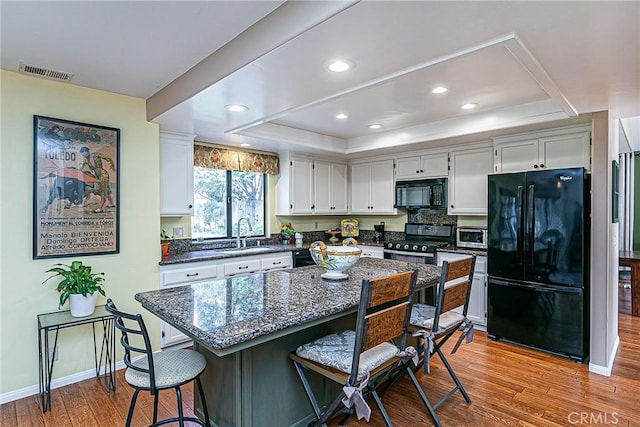 kitchen with black appliances, a raised ceiling, sink, white cabinetry, and light hardwood / wood-style flooring