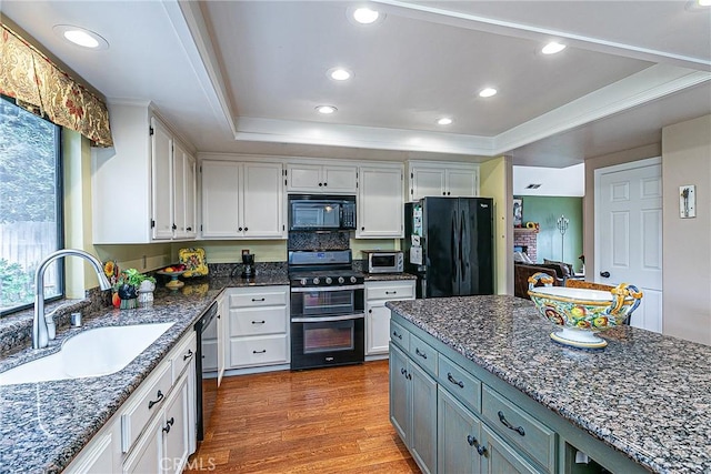 kitchen featuring a tray ceiling, white cabinets, black appliances, light hardwood / wood-style flooring, and sink