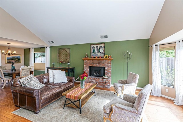 living room with light hardwood / wood-style floors, a brick fireplace, a notable chandelier, and vaulted ceiling