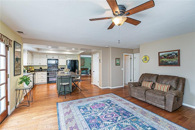 living room with ceiling fan, light hardwood / wood-style flooring, and a tray ceiling