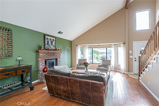 living room with a brick fireplace, hardwood / wood-style flooring, and high vaulted ceiling