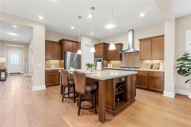 kitchen with decorative light fixtures, a breakfast bar, a kitchen island with sink, appliances with stainless steel finishes, and wall chimney exhaust hood