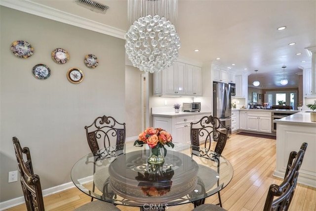 dining space with light hardwood / wood-style floors, ornamental molding, and an inviting chandelier