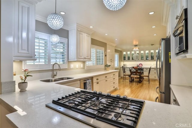 kitchen with white cabinetry, stainless steel appliances, hanging light fixtures, ornamental molding, and sink