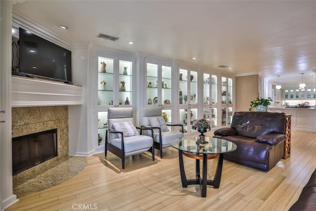 living room featuring light wood-type flooring, a premium fireplace, crown molding, and built in shelves