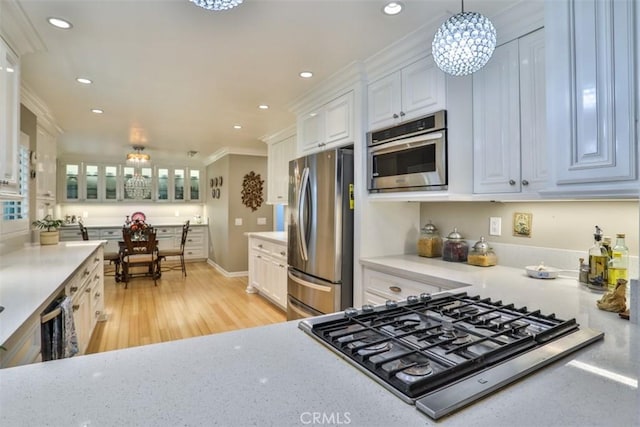 kitchen with white cabinetry, stainless steel appliances, an inviting chandelier, hanging light fixtures, and crown molding