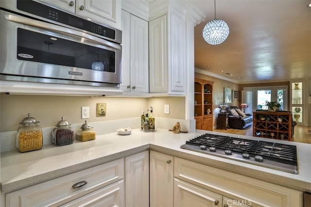 kitchen with pendant lighting, white cabinetry, stainless steel appliances, ornamental molding, and light stone counters