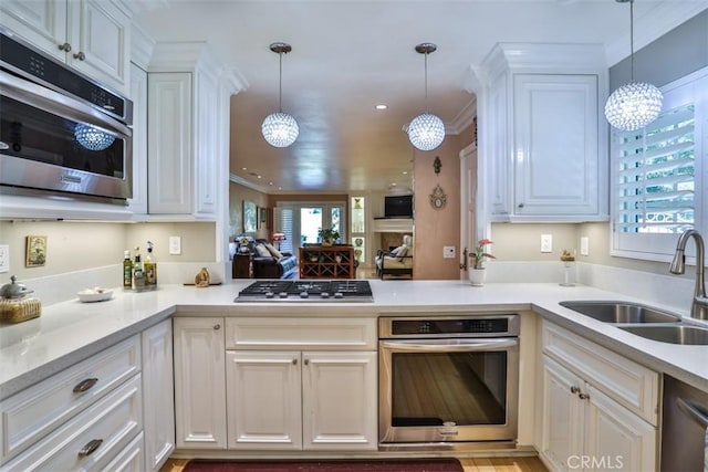 kitchen featuring pendant lighting, kitchen peninsula, sink, appliances with stainless steel finishes, and ornamental molding