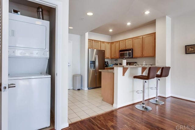 kitchen featuring kitchen peninsula, stacked washer / dryer, light wood-type flooring, appliances with stainless steel finishes, and a kitchen breakfast bar