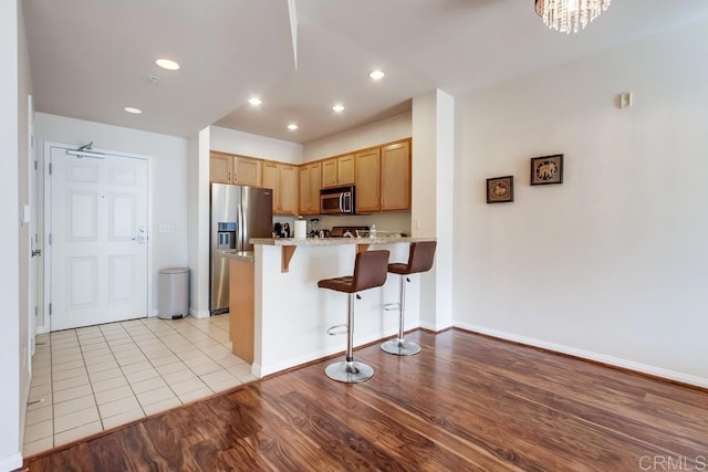 kitchen with kitchen peninsula, stainless steel appliances, a notable chandelier, light hardwood / wood-style flooring, and a breakfast bar