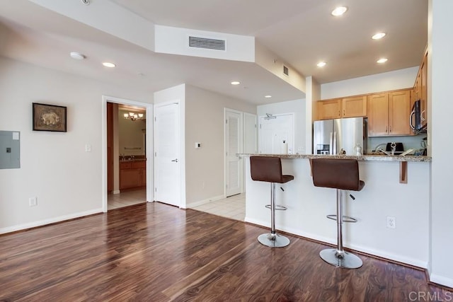 kitchen featuring stainless steel appliances, light hardwood / wood-style floors, kitchen peninsula, light stone counters, and a breakfast bar area