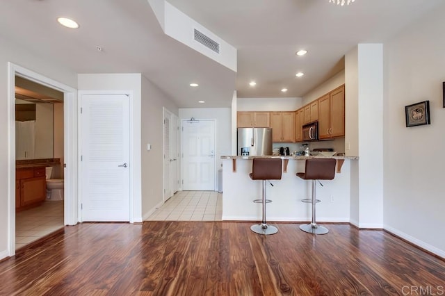 kitchen featuring kitchen peninsula, light hardwood / wood-style flooring, light stone countertops, a kitchen breakfast bar, and stainless steel appliances