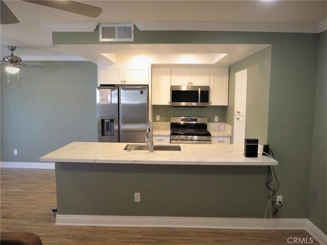 kitchen featuring kitchen peninsula, sink, white cabinetry, light stone countertops, and appliances with stainless steel finishes