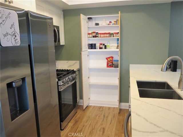 kitchen featuring light stone countertops, sink, stainless steel appliances, and light hardwood / wood-style flooring