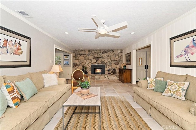 living room featuring a textured ceiling, a wood stove, light tile patterned flooring, ceiling fan, and crown molding