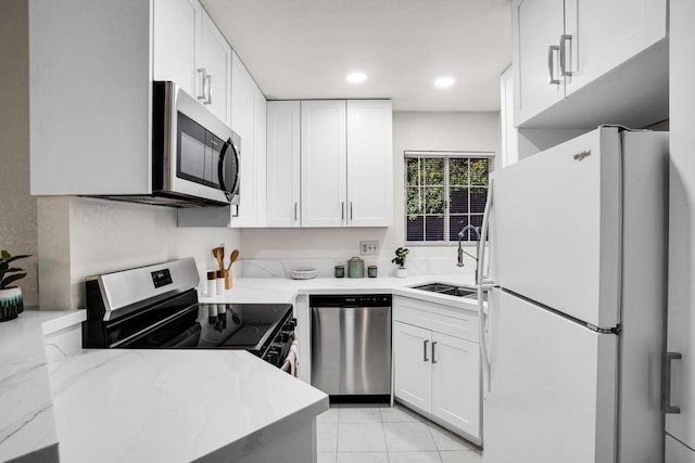 kitchen featuring light tile patterned floors, stainless steel appliances, white cabinets, light stone counters, and sink