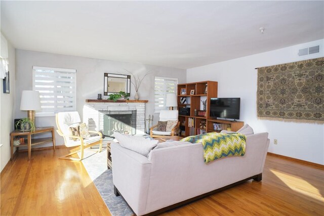 living room featuring a healthy amount of sunlight, a brick fireplace, and hardwood / wood-style flooring