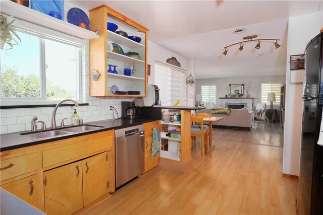 kitchen with tasteful backsplash, a brick fireplace, stainless steel dishwasher, sink, and light wood-type flooring