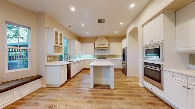 kitchen with appliances with stainless steel finishes, a center island, white cabinets, and custom range hood