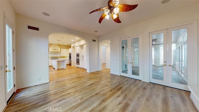 unfurnished living room with french doors, ceiling fan, and light hardwood / wood-style flooring