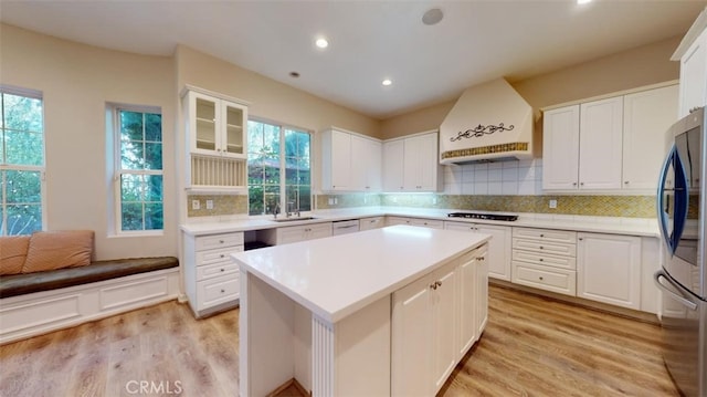 kitchen with custom exhaust hood, white cabinetry, sink, and stainless steel fridge