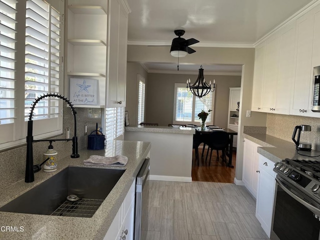 kitchen featuring appliances with stainless steel finishes, tasteful backsplash, ceiling fan with notable chandelier, white cabinets, and sink