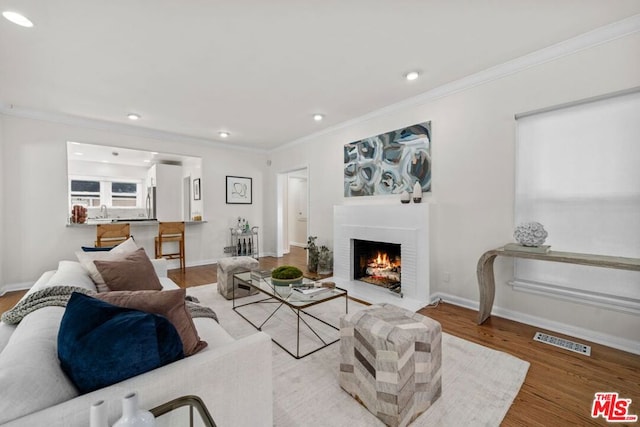 living room with a brick fireplace, light hardwood / wood-style flooring, and ornamental molding