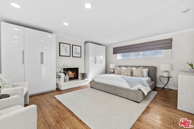 bedroom featuring a brick fireplace, crown molding, and light wood-type flooring