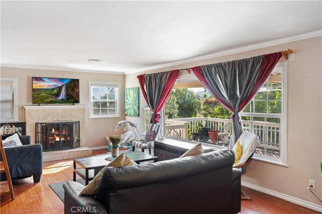 living room featuring crown molding, light hardwood / wood-style flooring, and a tile fireplace