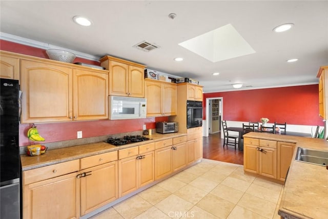 kitchen with light brown cabinetry, a skylight, light tile patterned floors, ornamental molding, and black appliances