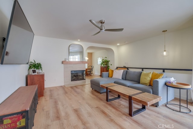 living room featuring light wood-type flooring, ceiling fan, and a tiled fireplace