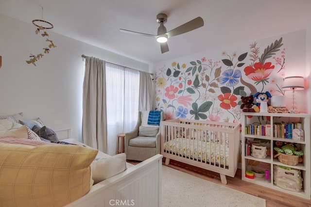 bedroom featuring ceiling fan, wood-type flooring, and a nursery area