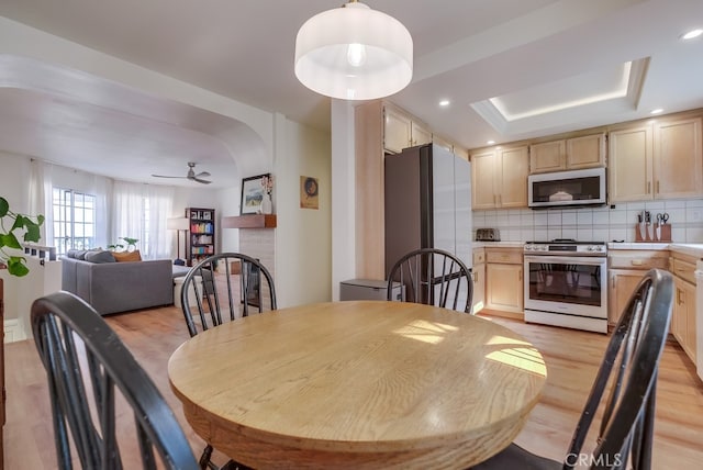 dining room featuring ceiling fan, a raised ceiling, and light wood-type flooring