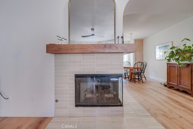 details with ceiling fan, a tiled fireplace, and wood-type flooring