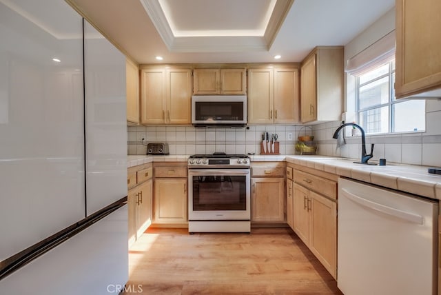 kitchen featuring tile counters, a raised ceiling, light brown cabinetry, gas range, and white dishwasher