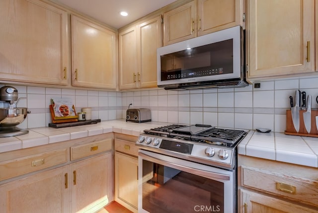 kitchen featuring light brown cabinets, appliances with stainless steel finishes, backsplash, and tile counters