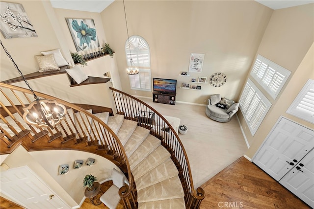 staircase with baseboards, a notable chandelier, a high ceiling, and wood finished floors