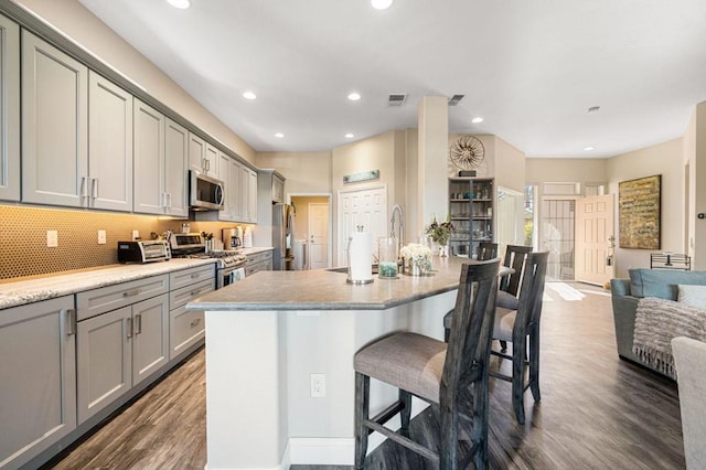 kitchen with dark wood-type flooring, appliances with stainless steel finishes, gray cabinetry, and a breakfast bar