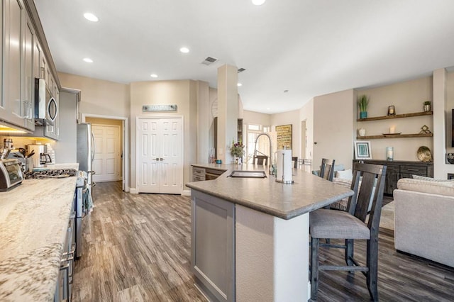 kitchen featuring gray cabinets, sink, dark wood-type flooring, appliances with stainless steel finishes, and a breakfast bar area