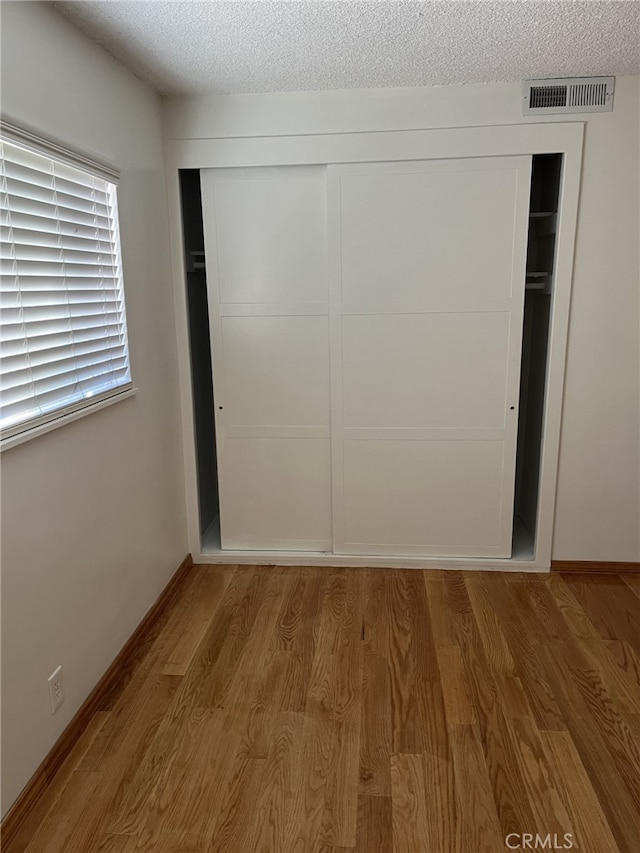 unfurnished bedroom featuring a textured ceiling, a closet, and light hardwood / wood-style flooring