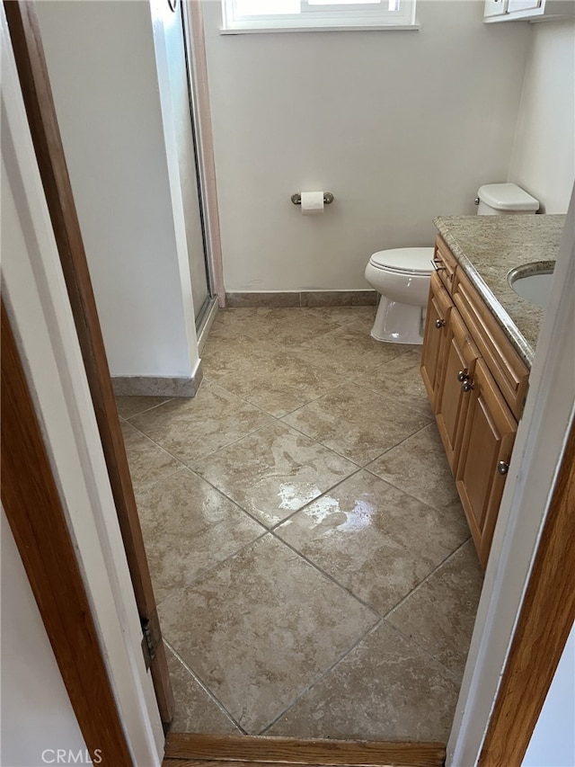 bathroom featuring toilet, vanity, and a shower with shower door