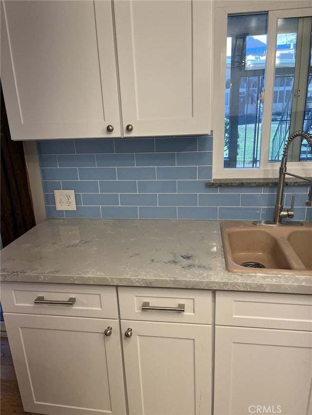 kitchen with light stone counters, white cabinets, tasteful backsplash, and sink