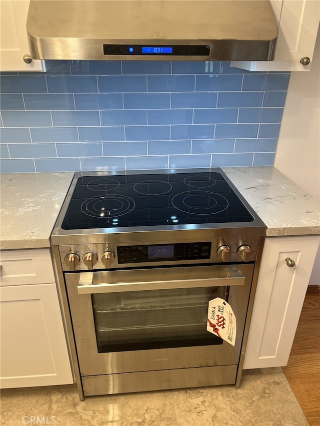 kitchen featuring light stone counters, white cabinetry, ventilation hood, and stainless steel range with electric stovetop