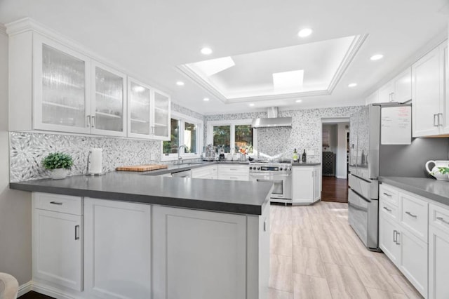 kitchen featuring appliances with stainless steel finishes, kitchen peninsula, a skylight, white cabinetry, and a tray ceiling