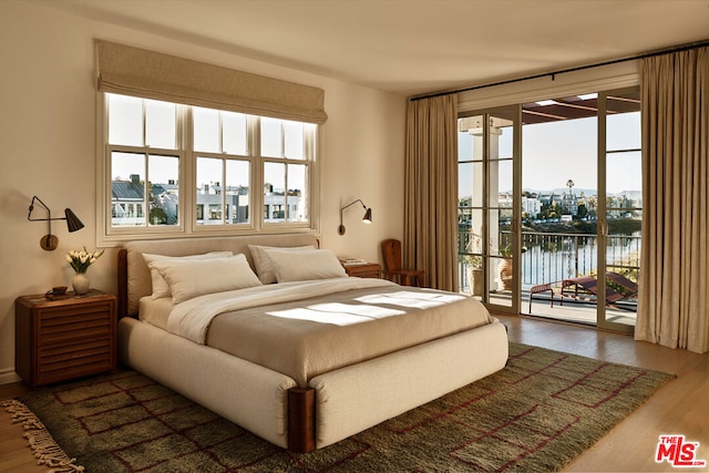 bedroom featuring dark wood-type flooring, access to exterior, and a water view