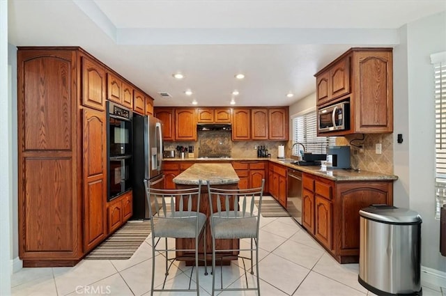 kitchen featuring light tile patterned floors, a breakfast bar area, tasteful backsplash, a kitchen island, and black appliances