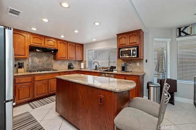 kitchen featuring appliances with stainless steel finishes, a kitchen island, tasteful backsplash, sink, and light tile patterned floors