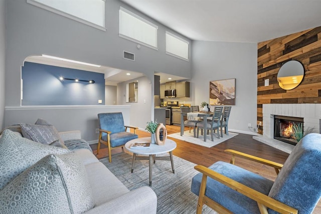 living room with hardwood / wood-style flooring, a brick fireplace, a high ceiling, and wooden walls