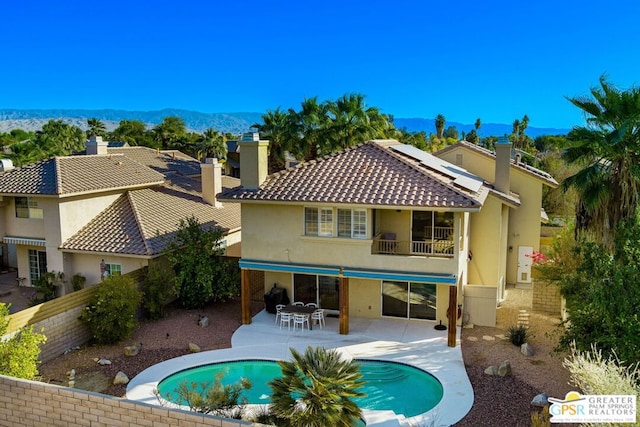 rear view of house featuring a mountain view, a patio area, a fenced in pool, a balcony, and solar panels