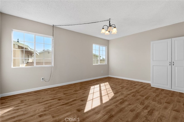 unfurnished room with a textured ceiling, a chandelier, and dark hardwood / wood-style flooring